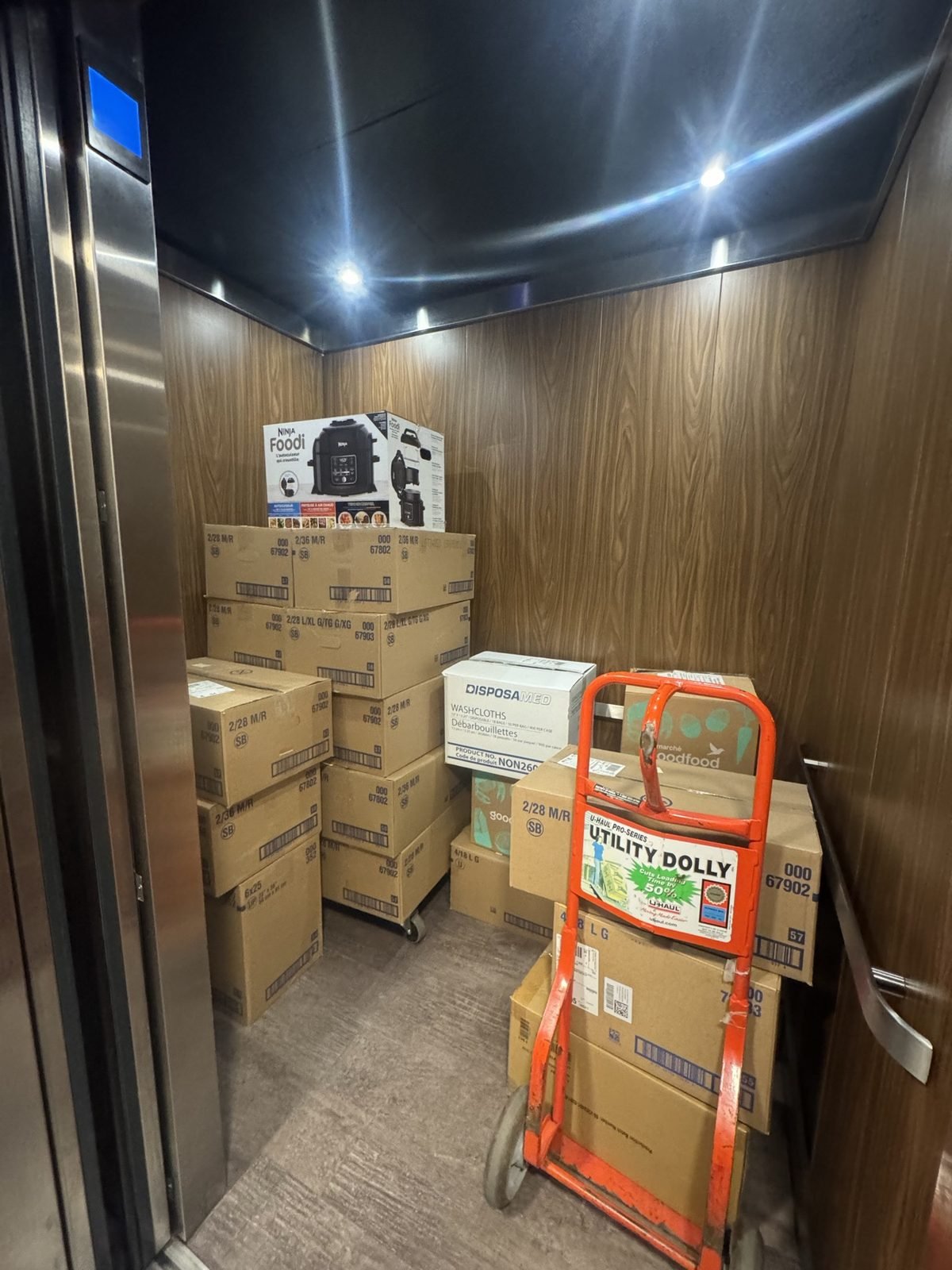 Boxes stacked in an elevator beside an orange utility dolly